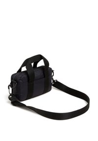 Black nylon bag with dual handles and adjustable strap. Features a rectangular shape with zip closure and textured surface.
