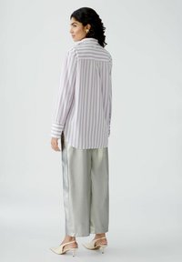 Striped button-up shirt in light lavender and white cotton, paired with metallic silver wide-leg pants. The outfit features a relaxed fit.