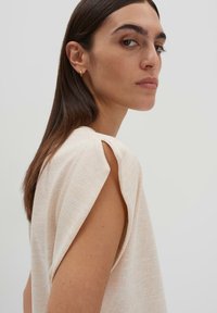 Top beige chiaro con maniche corte, realizzato in un tessuto morbido e texture. Sfumature di colore sottili offrono un aspetto stratificato e una vestibilità rilassata.