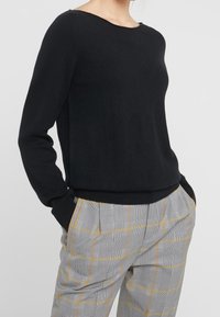 Pull en tricot noir avec un col rond et des manches longues. Associe à un pantalon à carreaux gris avec des accents jaunes et une coupe décontractée.