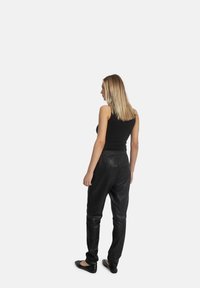 Sorte læderbukser med en afslappet pasform, elastisk talje og glat tekstur, parret med en sort tanktop og flade sorte sko.