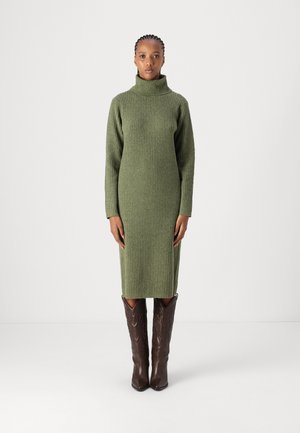 Robe en tricot côtelé vert olive avec un col haut et des manches longues, portée avec des bottes de cowboy brunes ornées d'un motif de couture détaillé.