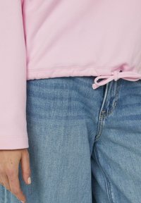 Jasnoróżowa bluza z długimi rękawami, z regulowanym ściągaczem w dolnej części. W zestawie luźne jasnoniebieskie jeansy.