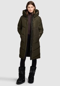Olive green puffer coat with a hood, zip closure, and stitched detailing, paired with black insulated boots featuring laces and a textured finish.