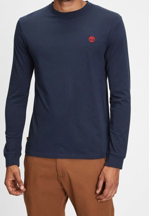 Navyblauw langarm T-shirt van katoen met een ronde hals. Voorzien van een klein rood logo op de borst en een recht gesneden zoom.