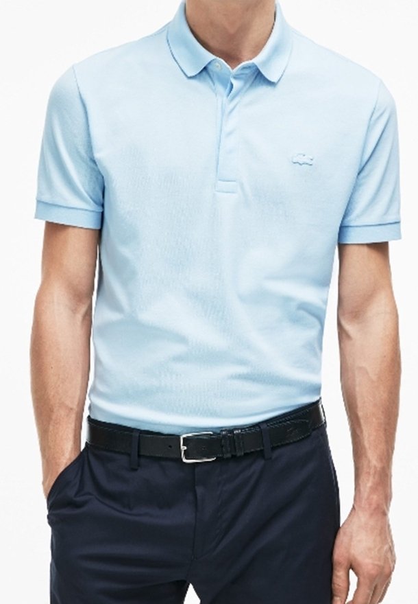 Ljusblå polo med krage, korta ärmar, texturerad tyg och broderad logotyp på bröstet. Bärs med marinblå byxor.