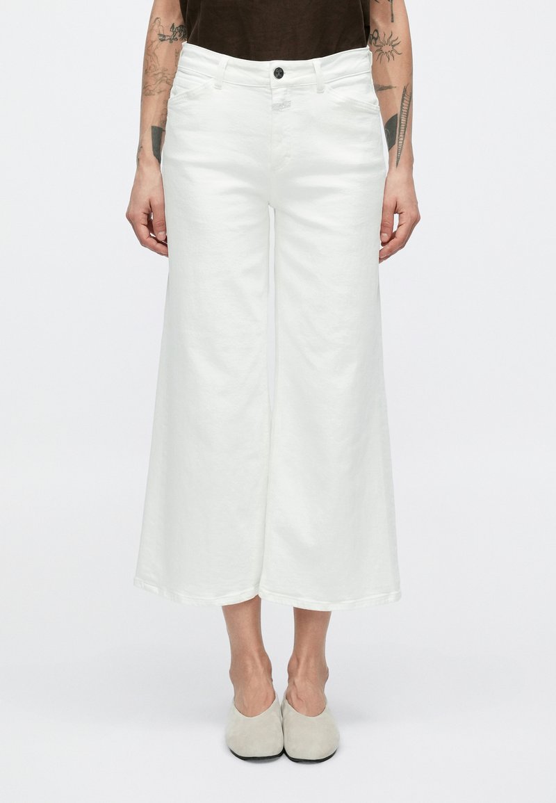 Άσπρο παντελόνι με φαρδιά γραμμή από βαμβάκι με υφή, διαθέτει μπροστινό κουμπί και λεπτομέρειες με τσέπες. Το τελείωμα φτάνει μέχρι το μέσο του μοσχαριού.