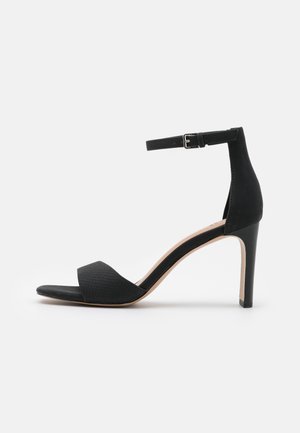 Sandal à talons hauts noirs avec une bride à la cheville et une boucle, bout ouvert, bande frontale texturée, contrefort lisse et talon aiguille fin.