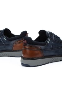 Zapatos de cuero con una parte superior en azul marino oscuro y detalles en cuero marrón. Presentan una suela de goma texturizada y un forro textil. Acabado liso con detalles de costura.