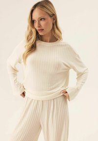 Ribbed cream sweater with long sleeves, round neck, and relaxed fit paired with matching ribbed pants. Soft texture and comfortable design.