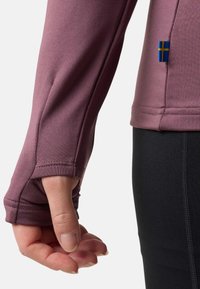 Top a maniche lunghe e aderente in tessuto mauve polveroso, con aperture per il pollice ai polsini e un piccolo accento della bandiera svedese sul lato.
