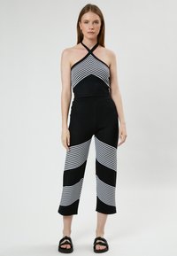 Zwart-witte gestreepte haltertop, gecombineerd met zwarte wijd-uitlopende broek met een golvend streep patroon. Soepele, rekbare breistekstof.