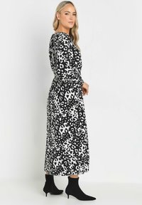 Schwarz-weißer gemusterter Maxikleid mit langen Ärmeln, tailliertem Bund und leichtem Fall, kombiniert mit schwarzen Stiefeletten. Glatte Stoffstruktur.