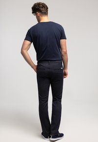 Granatowy T-shirt z krótkim rękawem, zestawiony z ciemnymi jeansami. Spodnie mają delikatny połysk, dwie tylne kieszenie i dopasowany krój.