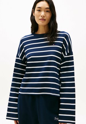 Maglia a maniche lunghe blu navy con strisce orizzontali bianche, dotata di collo a giro e un piccolo logo. Tessuto di cotone morbido.