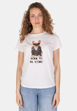 Donna con capelli ricci che indossa una maglietta bianca con un cane con occhiali da sole e giacca di pelle con la scritta "Born to be iconic", abbinata a jeans blu.