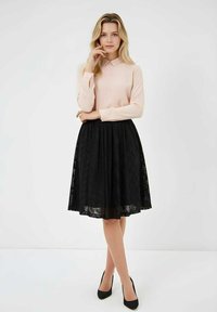 Blusa de manga larga de color rosa claro con cuello, combinada con una falda línea A de encaje negro, por encima de la rodilla, y zapatos de tacón altos negros.