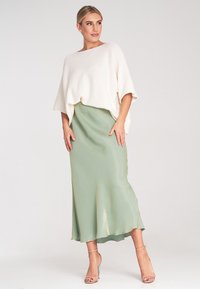 Cremfarbener Strickoberteil mit weiten Ärmeln, kombiniert mit einem fließenden, mintgrünen Satrock mit einem zarten Glanz und Schleppe. Klare hohe Schuhe.