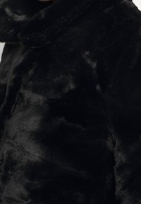 Veste en fausse fourrure noire avec une texture douce et moelleuse, dotée d'un col arrondi et d'un design élégant, présentant une couleur uniforme et un minimum de détails.