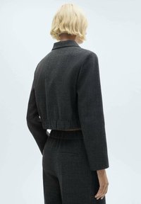 Afskåret sort og grå plaidjakke med lange ærmer, featuring en krave og elastisk bund. Glat tekstur, struktureret design, minimal detaljering.