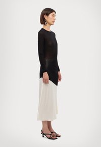 Must have pikad varrukad must topp, mis on paaritatud kreemika, asümmeetrilise midi seeliku abil. Kostiilil on sile tekstuur ja minimalistlik disain.