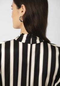 Black and white vertically striped blouse with a high collar and back zipper detail. Smooth, shiny fabric with contrasting stripes.
