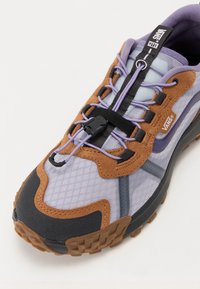Vans-fottøy har en lys lilla mesh-overdel, brune semsket skinn-overlegg, et svart snøring-system og en teksturert gummisåle for grep.
