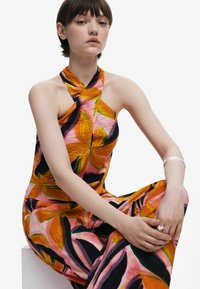 Jumpsuit colorato con scollatura a halter, caratterizzato da un motivo floreale in arancione, rosa e nero. Il tessuto appare leggero con una texture increspata.