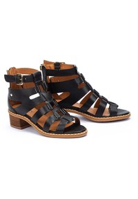 Sandalias de tacón de piel negra con tiras horizontales y verticales, punta abierta, forro interior marrón y tacón de bloque de madera clara.