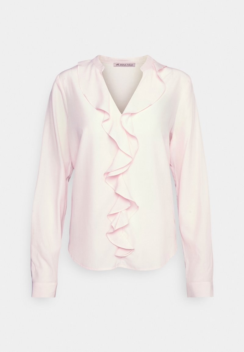Blouse rose clair à manches longues avec col en V et détail volanté en cascade au centre devant.
