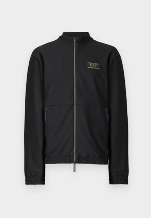 Giacca nera con zip e tessuto strutturato, caratterizzata da un collo alto, polsini elastici e un logo dorato sul petto. Design leggero.