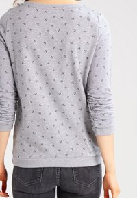 Camiseta gris de manga larga con patrón de anclas en azul marino, escote redondeado y puños acanalados. Combina con jeans gris oscuro. Diseño tipo pulóver.