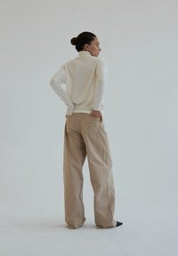 Kremowy sweter z golfem zestawiony z beżowymi spodniami o szerokich nogawkach, z charakterystycznym wzorem i minimalistycznym stylem. Widok z tyłu.