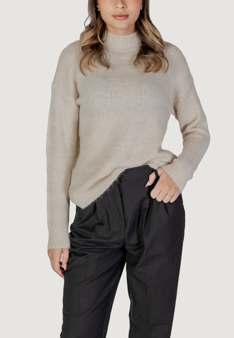 Hellbeige gestrickter Pullover mit hohem Kragen, lässiger Passform und seitlichen Schlitzen. Tragen mit schwarzen, hochgeschnittenen Hosen. Weicher, strukturierten Stoff.