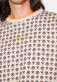Maglione beige con un motivo ripetuto di icone marroni e un colletto a coste arancione. Testo "CARLO COLUCCI" in arancione sul davanti.