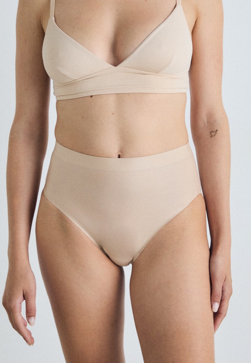 Beige bh met een driehoekige vorm en brede bandjes, gecombineerd met hoge beige slipjes. Beide hebben een gladde, zachte textuur.