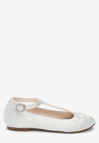 Ballerine en satin blanc avec une lanière T et boucle, ornée de petites fleurs et perles sur le devant, et une semelle marron.