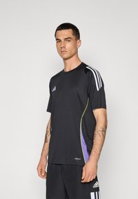 Svart treningstrøye med korte ermer, med hvite tre-stripe detaljer, grønne og lilla sidepaneler, og "AEROREADY" etikett.