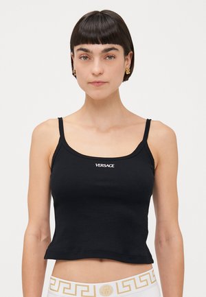 Débardeur noir à côtes avec des bretelles fines, présentant le lettrage blanc "VERSACE" à l'avant. La coupe est courte et ajustée, mettant en valeur le torse.