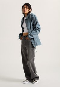Helle blaue übergroße Jacke, weißes Crop-Top, graue hochsitze Jeans und schwarz-weiß karierte Slipper. Glatter Stoff und lässige Passform.