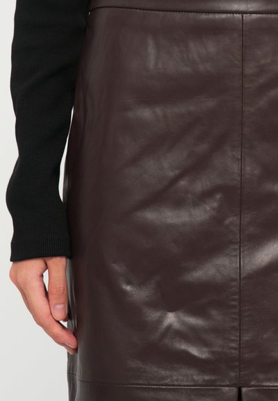Person wearing a dark brown leather skirt and a long-sleeve black ribbed top, hand resting beside the skirt.