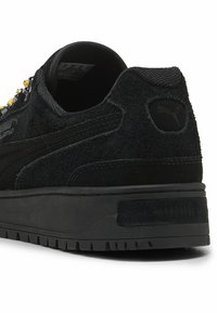 Zwarte suède sneakers met een gestructureerd oppervlak, rubberen zool, gouden hardware-accenten en het Puma-logo op de hiel. Laag-top ontwerp met een ronde vorm.