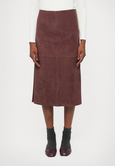 Falda midi de ante malva con una silueta recta, detalles de costura y aberturas laterales. Combinada con calcetines grises y zapatos burdeos.