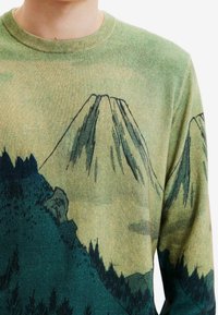 Stickad tröja med ett grönt landskapsmönster som föreställer berg och träd. Texturen är mjuk, med detaljerad konst i mörkgröna och beige toner.