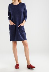 Navyblå stickad klänning med långa ärmar, två framfickor och en avslappnad passform. Matchad med röda slip-on skor med spetsig tå.