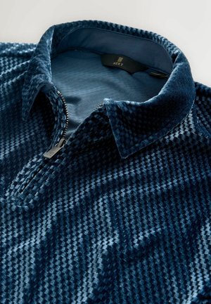 Tamsiai mėlynas užtraukiamas puloveris, pagamintas iš tekstūrinio veliūro, su raštuotu paviršiumi, apykakle ir sidabriniu užtrauktuku.