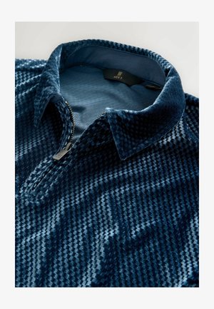 Navyblauer Zip-Up-Pullover aus strukturiertem samtigem Material mit gemusterter Oberfläche, Kragen und silbernem Reißverschlussdetail.