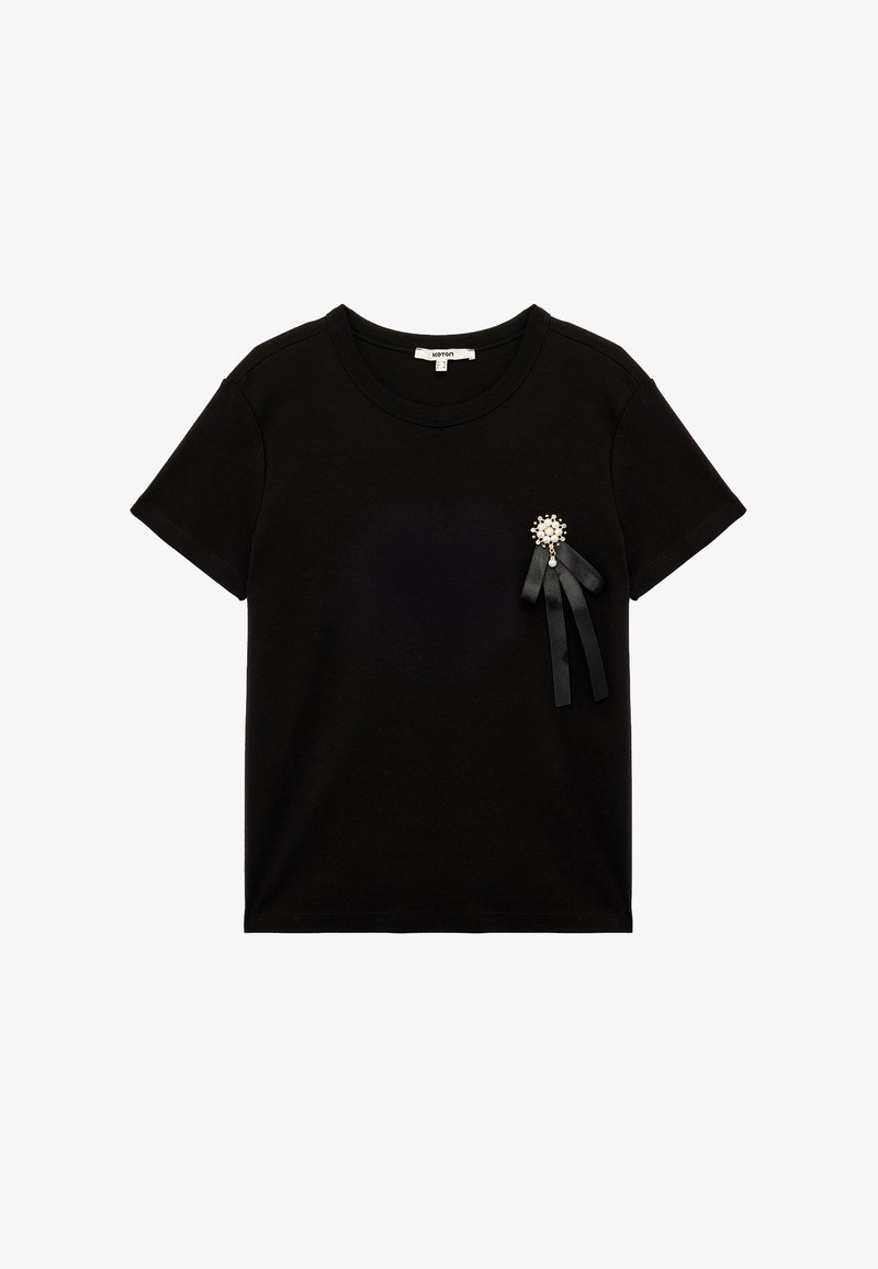 Mustat puuvillapaidat, joissa on lyhyet hihat, pyöreä kaula-aukko ja koristeellinen rintaneula, jossa on helmiläikkä ja mustat nauhaaksentit.