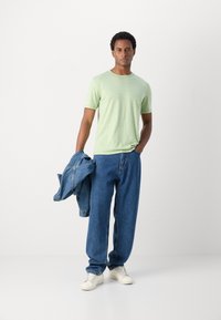 Un tricou scurt cu mânecă scurtă de culoare verde deschis, blugi lejeri albastri, adidași albi și o jachetă din denim aruncată pe braț. O ținută simplă și lejeră.