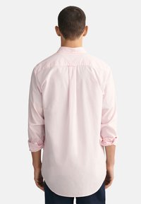 Helles rosa Hemd mit langen Ärmeln, leicht an den Bündchen aufgerollt, mit einer sanften Textur und abgerundetem Saum.